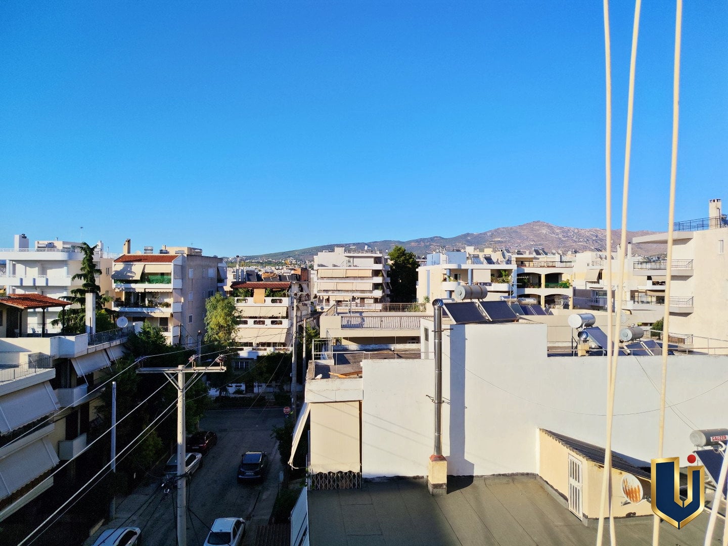 Θέα προς την Πεντέλη από το μπαλκόνι – Ρετιρέ Μαρούσι | 150-1051 Θέα από το μπαλκόνι προς τις πολυκατοικίες του Αμαρουσίου, με το όρος Πεντέλη στο βάθος και καθαρό γαλανό ουρανό.